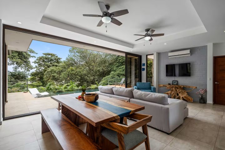 Open living room with patio view, wooden dining set, white sofa, TV, and ceiling fans.