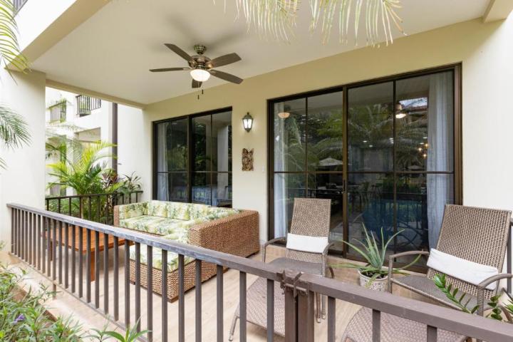 Covered patio with chairs, wicker sofa, ceiling fan, and potted plants overlooking greenery.