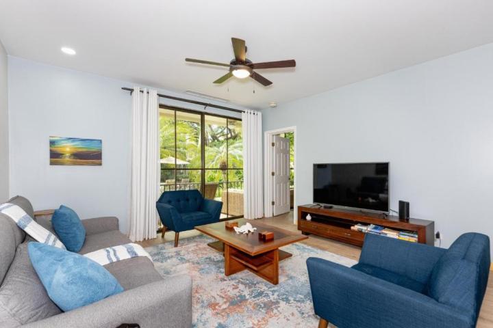 Modern living room with blue chairs, gray sofa, TV, wooden coffee table, and large window with garden view.