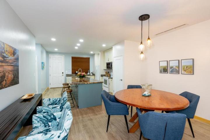 Open kitchen and dining area with blue chairs, round table, hanging lights, and artwork on walls.