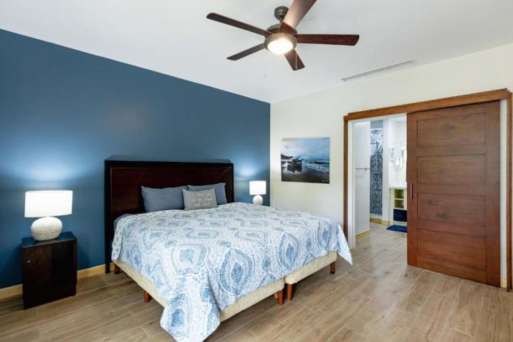 Bedroom with blue wall, bed, nightstands, ceiling fan, and open door to bathroom.