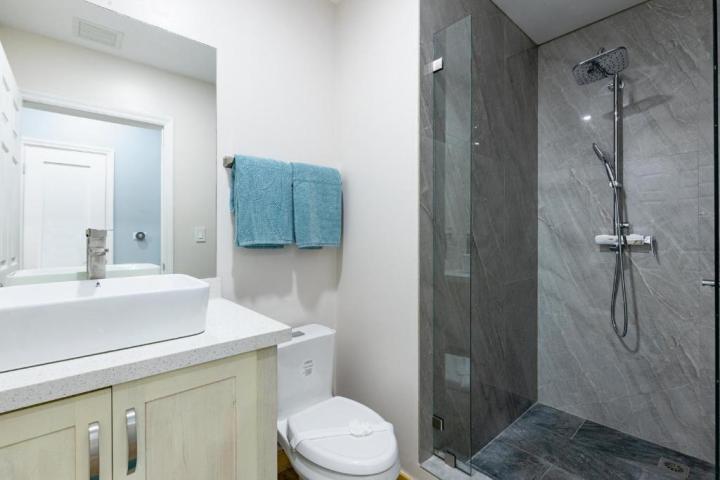 Modern bathroom with white sink, toilet, gray-tiled shower, and blue towels.
