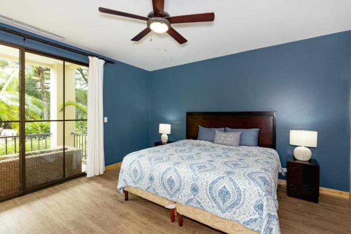 Bedroom with blue walls, ceiling fan, large bed, and glass doors to balcony.