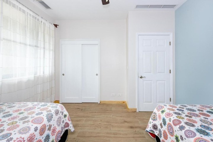 Bedroom with two beds, patterned quilts, white closet doors, and light curtains on the window.
