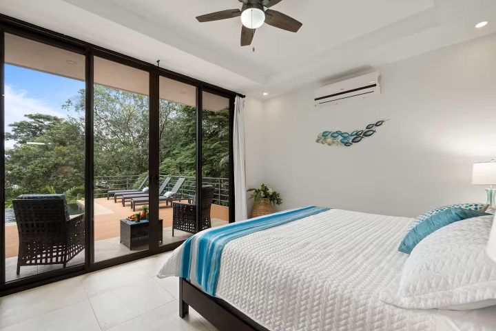Bedroom with sliding glass doors to a balcony, bed, and ceiling fan, overlooking trees.
