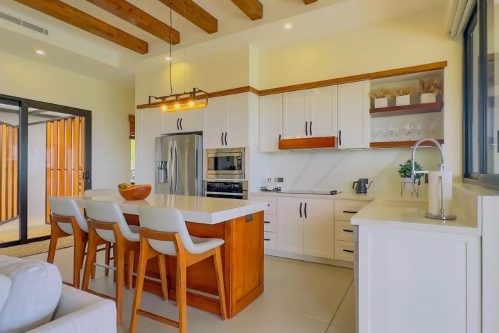 Modern kitchen with island, bar stools, stainless steel appliances, and wooden ceiling beams.