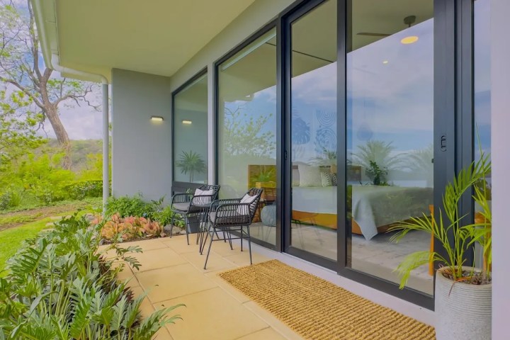 Modern patio with two black chairs, glass doors, and lush greenery.