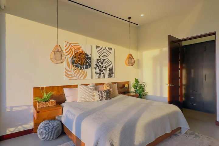 Modern bedroom with a wooden bed, abstract wall art, and hanging wicker lamps.