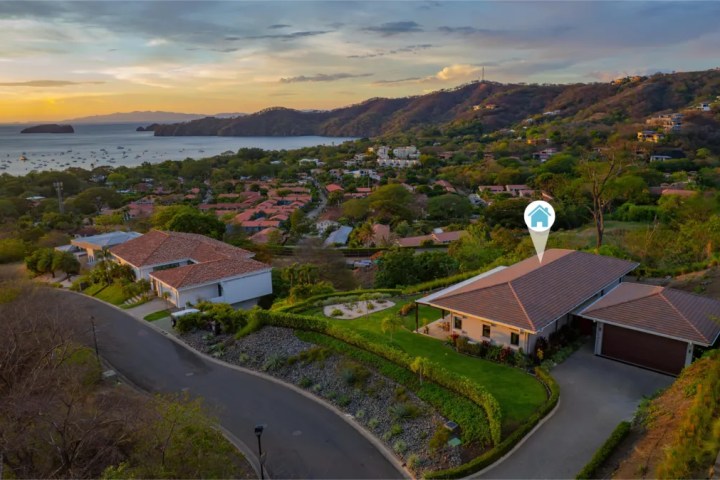 A house with a pool in a hilly coastal neighborhood at sunset.