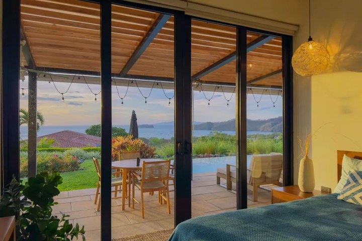 Bedroom with sliding glass doors to a patio, ocean view, and sunset lighting.