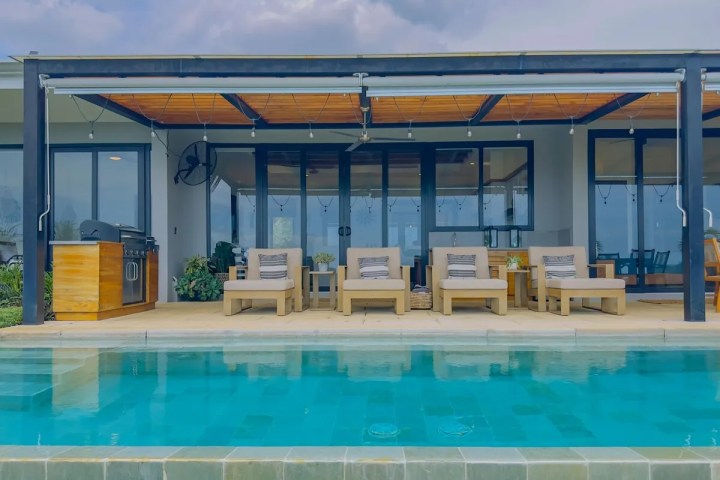 Modern patio with lounge chairs and pool, under cloudy sky.