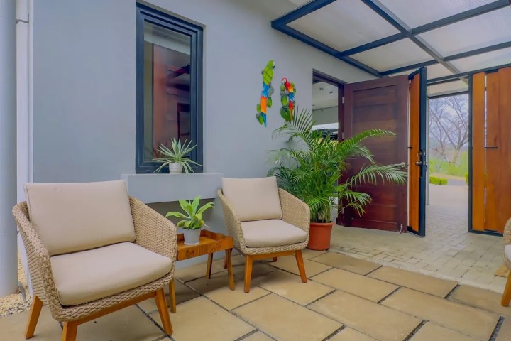 Outdoor patio with two wicker chairs, plants, and an open wooden double door.