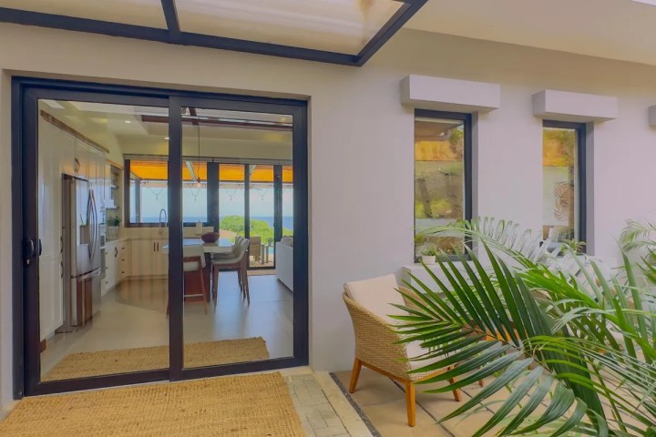 Modern patio with sliding glass doors, plants, and wicker furniture leading to a bright kitchen.