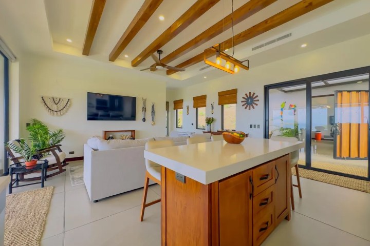 Modern open living space with kitchen island, wooden beams, and large windows.