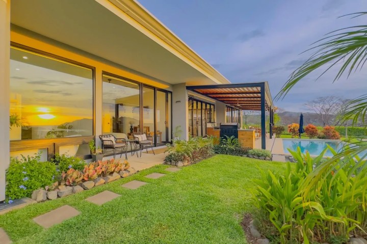 Modern house with pool, patio, and garden at sunset.
