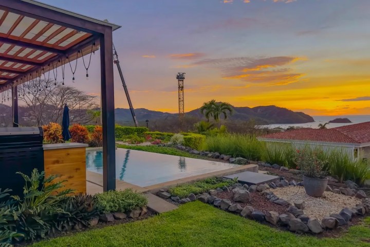 Scenic view of a poolside terrace with a mountain and ocean sunset backdrop.
