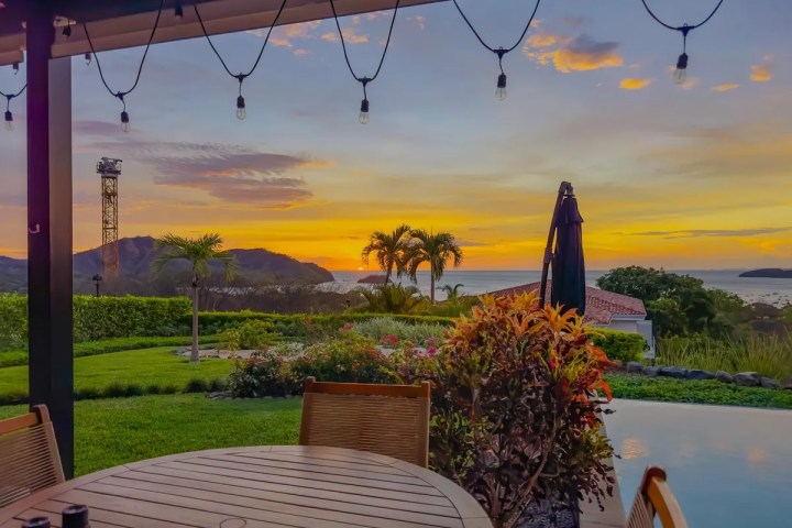 Patio with table, plants, and view of sunset over ocean and hills.