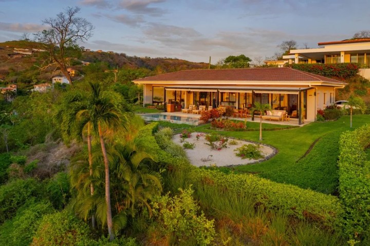 A modern house with large windows on a hillside surrounded by lush greenery.