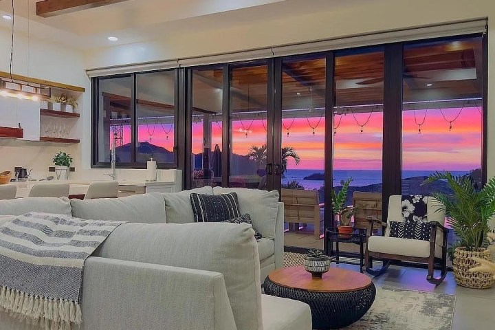 Modern living room with gray sofas, coffee table, and large windows showing a vibrant sunset view.