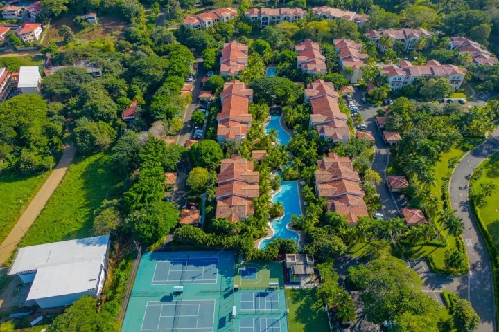 Aerial view of red-roofed buildings and two tennis courts surrounded by greenery.