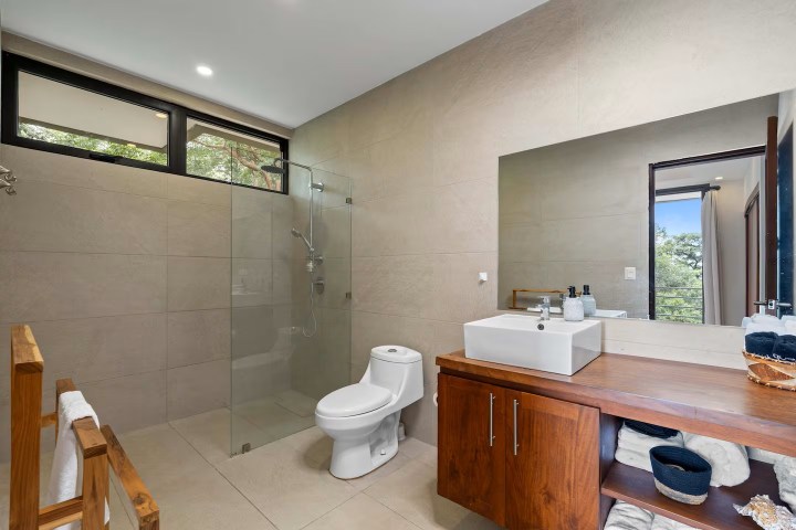 Modern bathroom with glass shower, toilet, large mirror, and wooden vanity with sink.