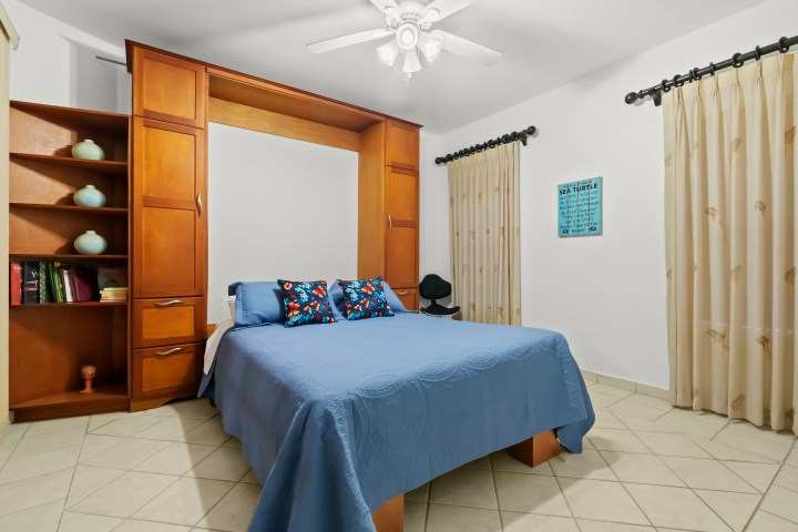 Bedroom with a blue bedspread, wooden shelves, and a ceiling fan.