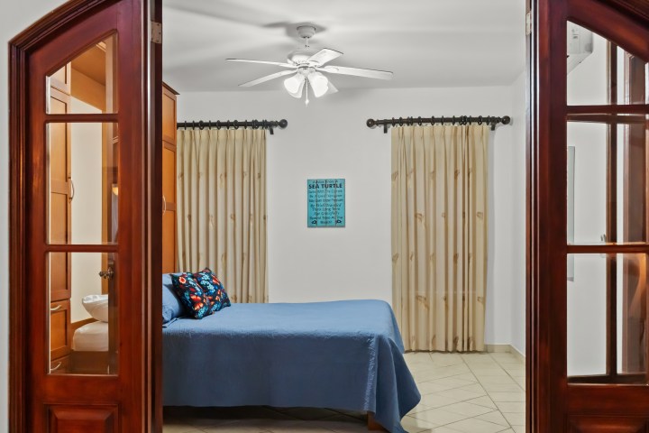 Bedroom with wooden doors, blue bedding, cream curtains, and wooden furniture.