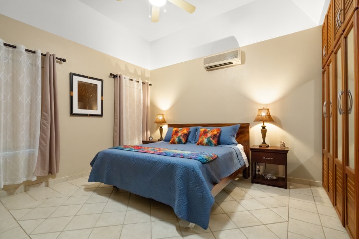 Cozy bedroom with blue bedspread, nightstands, lamps, and wooden closet.