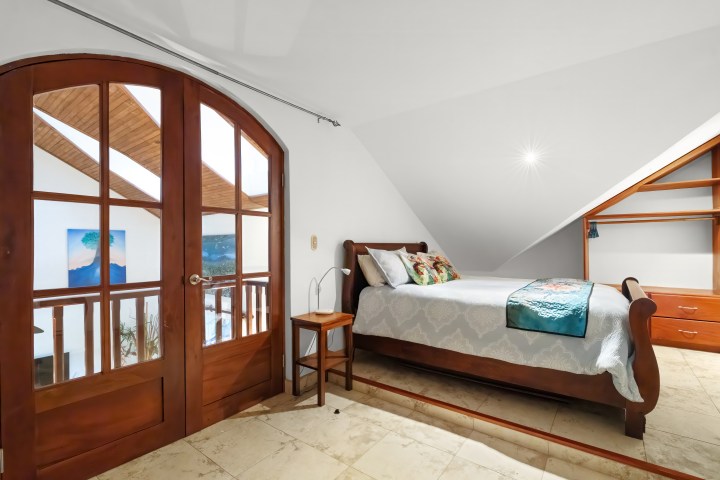 Cozy attic bedroom with a wooden bed, side table, and arched window.