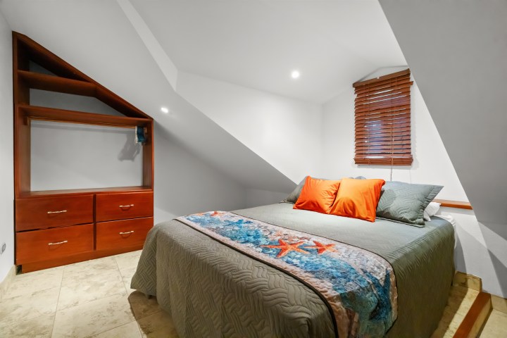 Attic bedroom with a bed, colorful pillows, wooden drawers, and a sloped ceiling.
