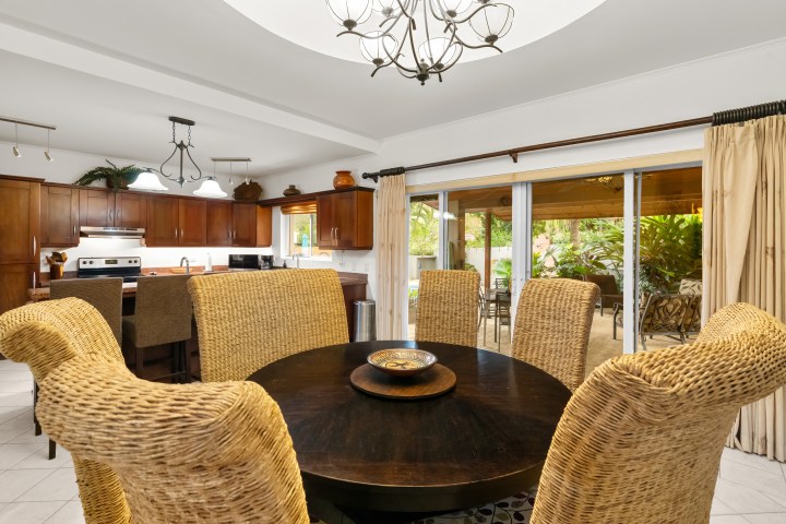 Dining area with wicker chairs and round table, kitchen in background, sliding doors to patio.