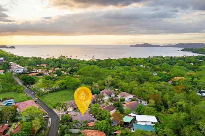 Aerial view of a coastal town with lush greenery and ocean at sunset.
