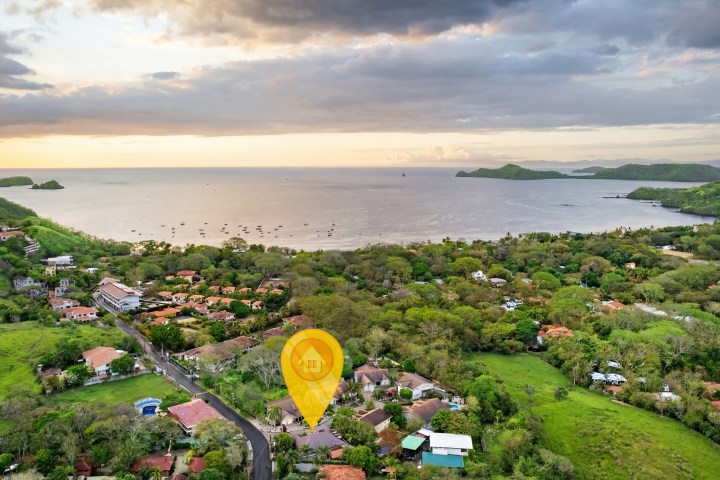 Coastal town with lush greenery and ocean view at sunset, pin marking a location.