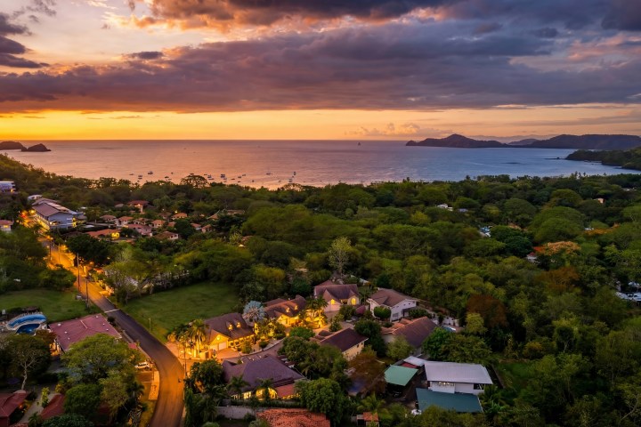 Aerial view of a coastal town at sunset with a bay and scattered houses.