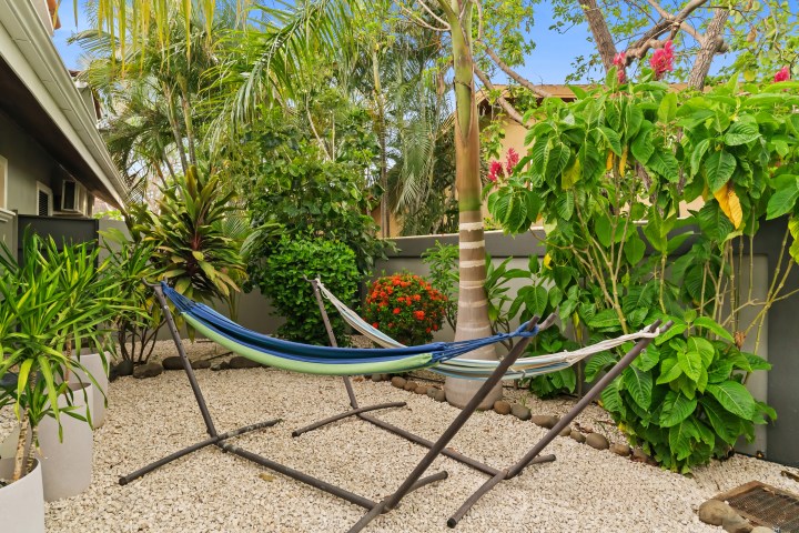 Hammock on stand in garden with palm trees and lush greenery.