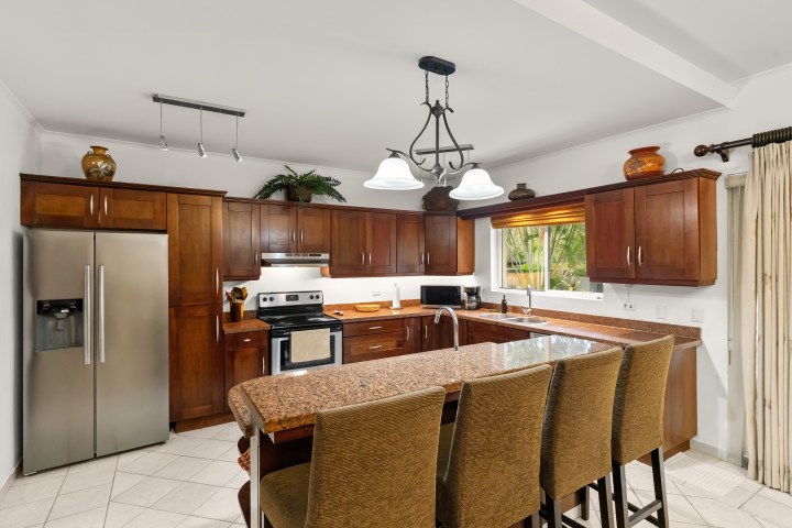 Modern kitchen with wooden cabinets, stainless steel appliances, and a large granite island with bar stools.
