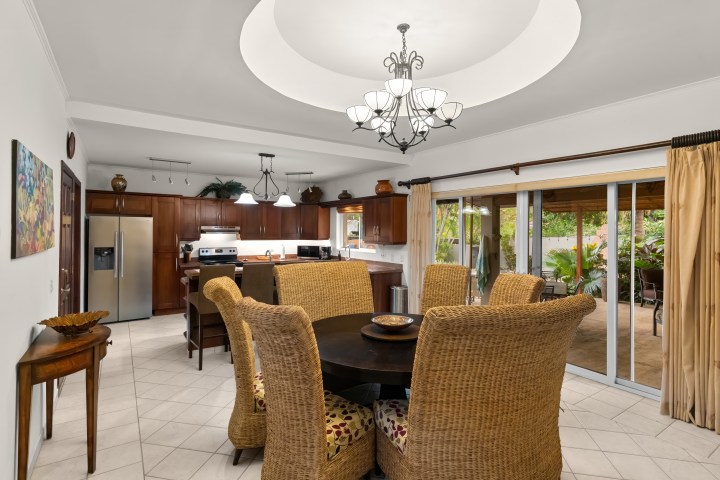 Dining room with wicker chairs, round table, chandelier, and view of kitchen and patio.