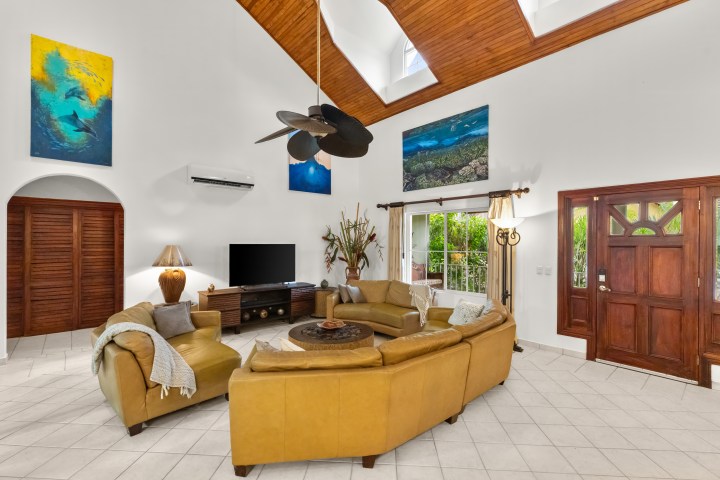 Bright living room with yellow sofas, TV, large art, and wooden ceiling fan.