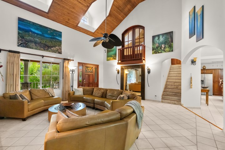 Spacious living room with tan sofas, high ceiling, art, and staircase.