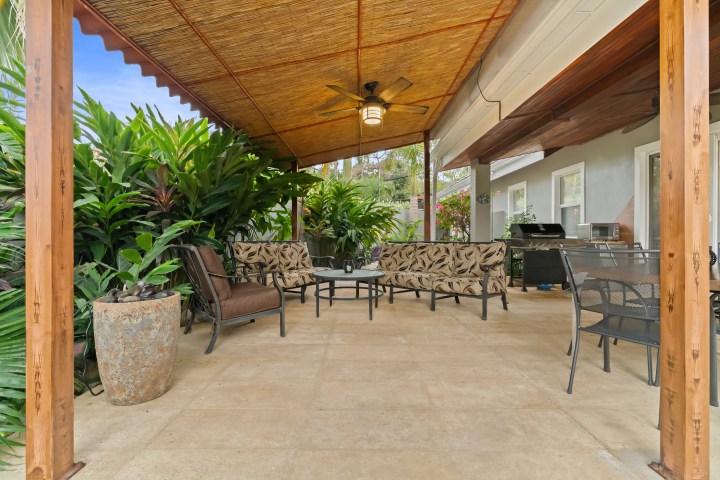 Outdoor patio with furniture under a wooden pergola and lush greenery.
