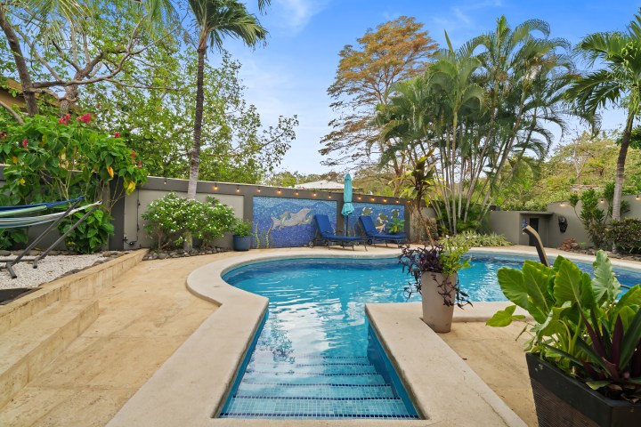 Outdoor pool with lounge chairs, surrounded by lush greenery and decorative wall.