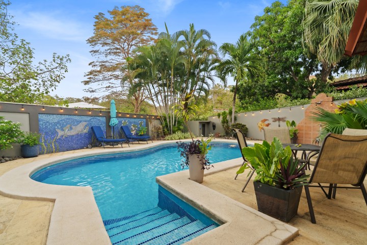 Tropical backyard with pool, plants, and patio furniture.