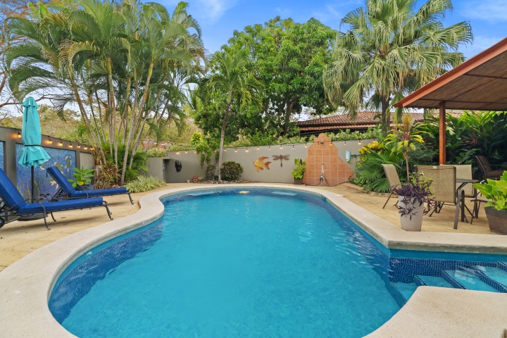 Tropical backyard pool with lounge chairs and greenery.