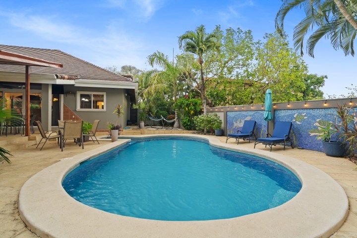 Backyard pool with patio, lounge chairs, and tropical plants.