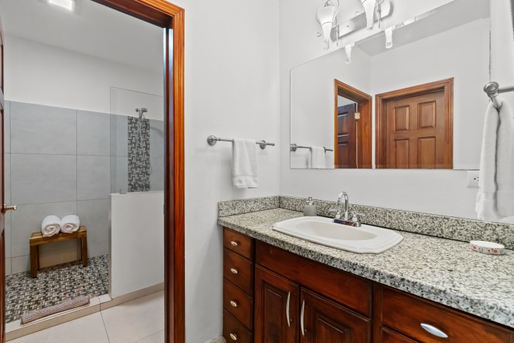 Bathroom with a granite countertop, wooden cabinet, shower, and towel rack.