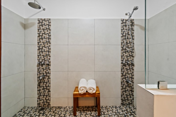 Modern shower room with dual showers, tiled walls, and a wooden bench holding two rolled towels.
