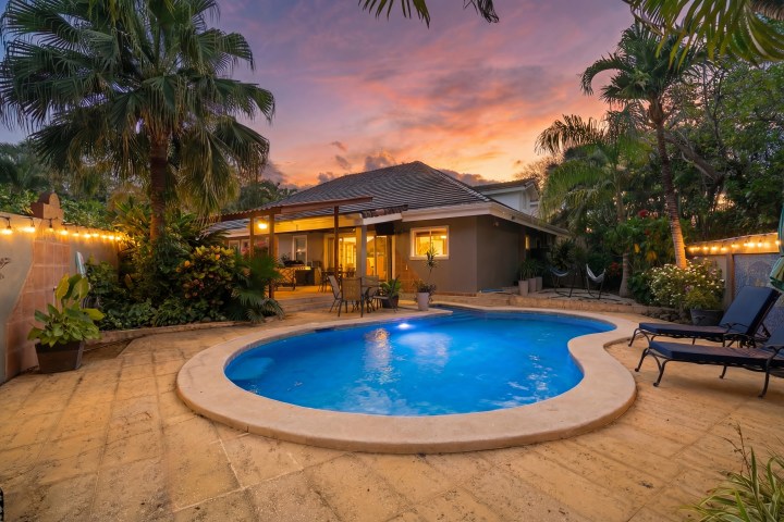 Backyard pool area at sunset with patio, string lights, and lounge chairs.