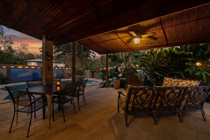 Covered patio with seating overlooking a pool at sunset.