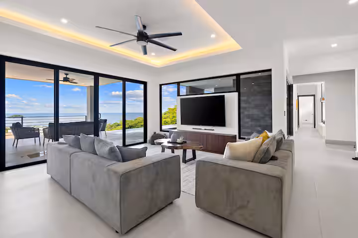 Modern living room with gray sofas, TV, and ocean view through large glass doors.