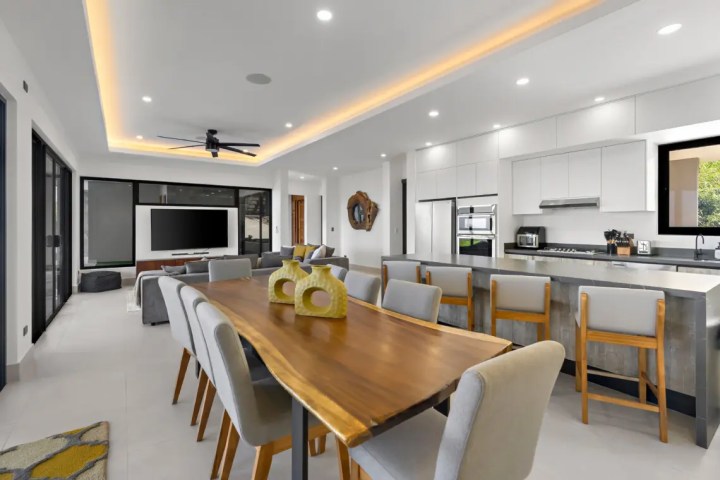 Modern open-plan living room and kitchen with dining table and bar stools.